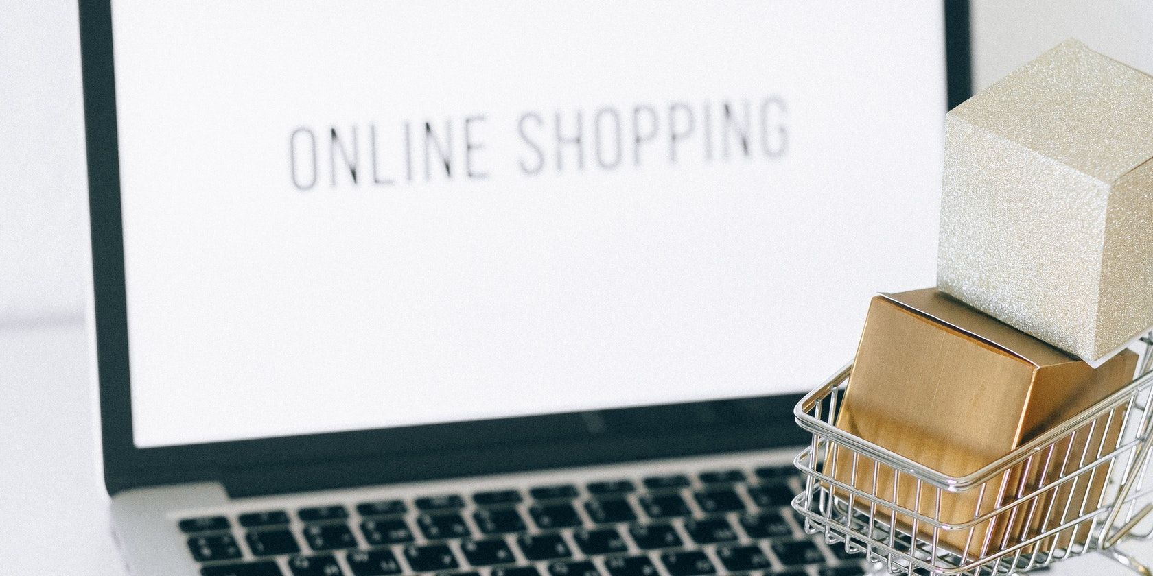 Picture of a laptop with online shopping written on its screen, and a model shopping cart nearby
