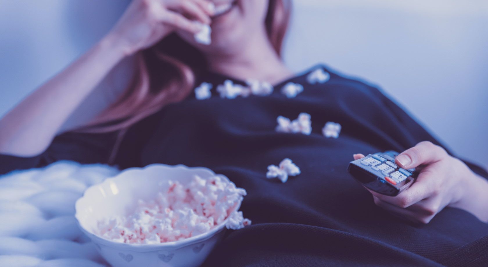 Laughing woman eating popcorn in bed and watching movies