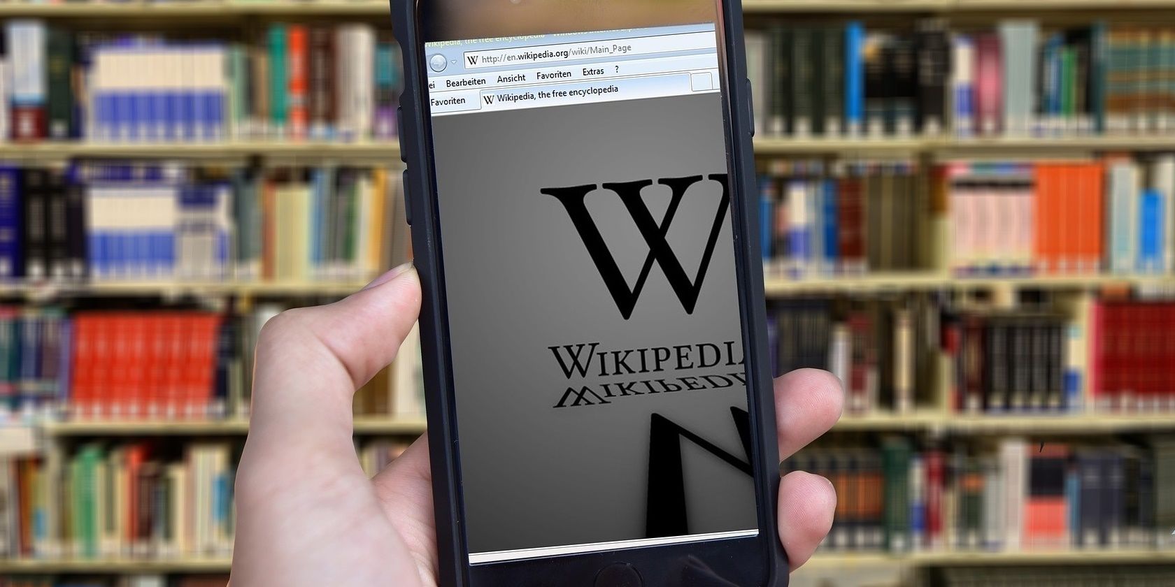 Hand holding phone with Wiki page loaded in front of bookcase