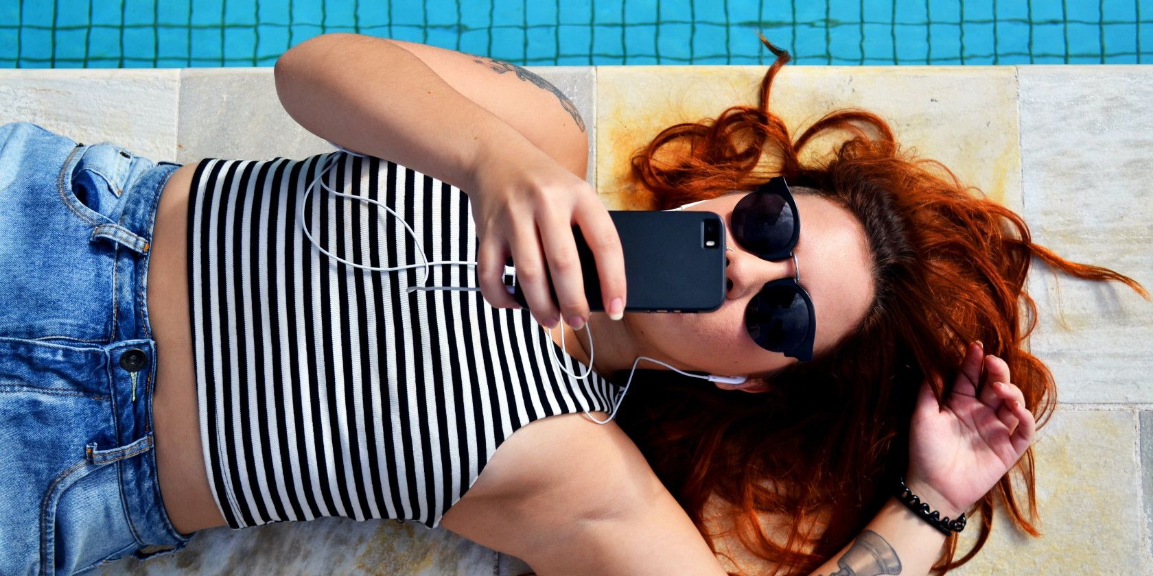 Woman lying down next to pool using smartphone