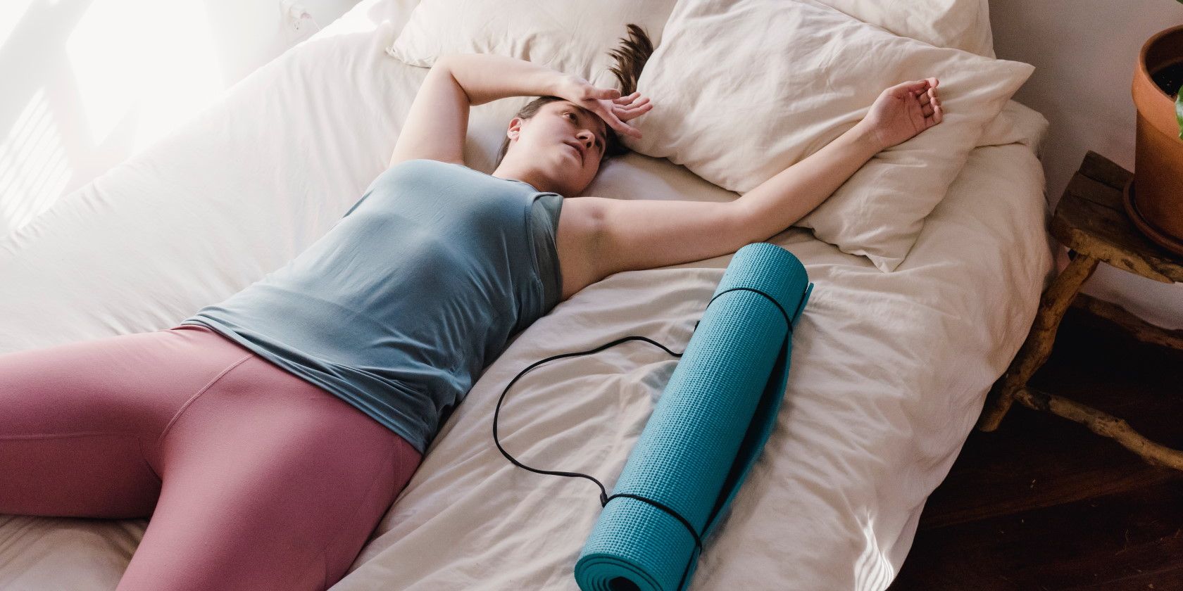 tired woman resting on bed next to exercise mat