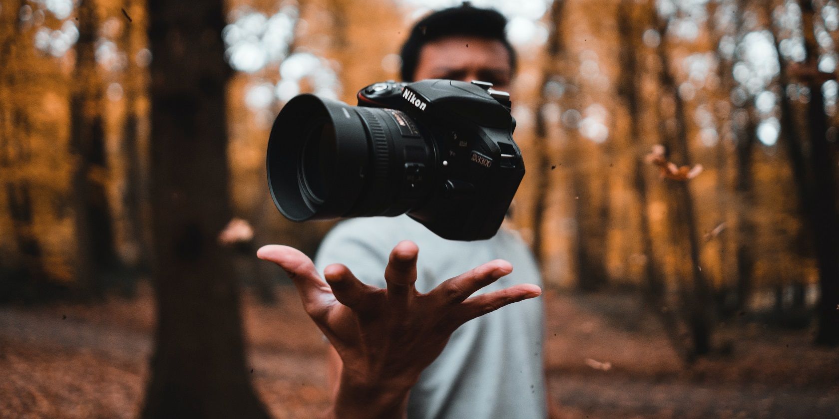 A man tossing a Nikon camera up in a forest
