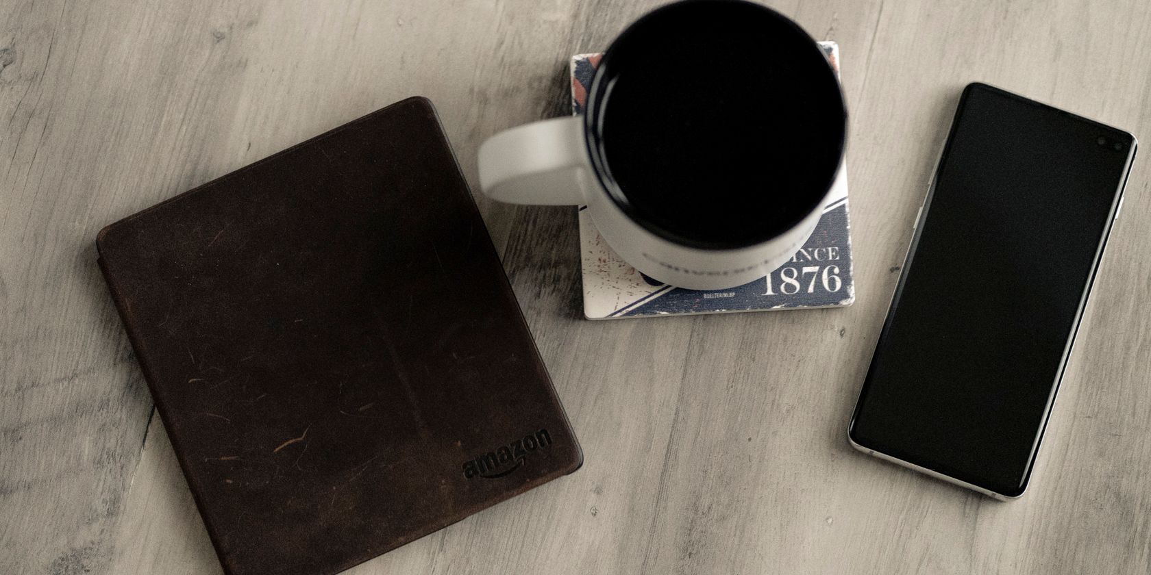 Photo of a Kindle oasis on a desk with a smartphone and a mug