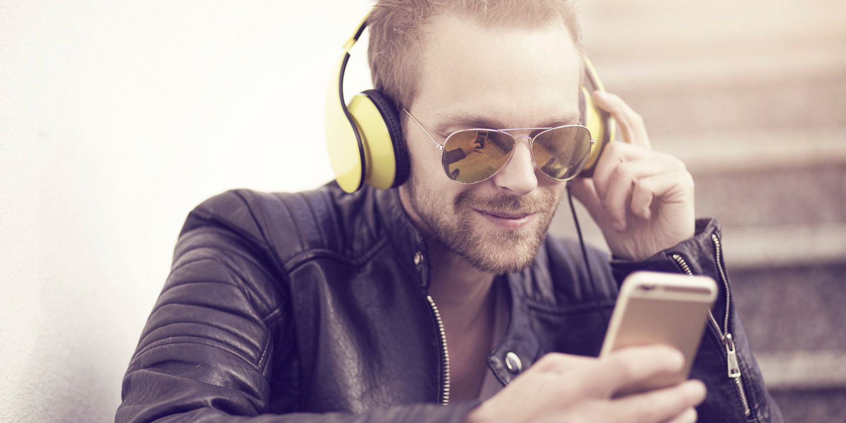 Photo of a man wearing sunglasses listening to music through headphones while looking at a phone