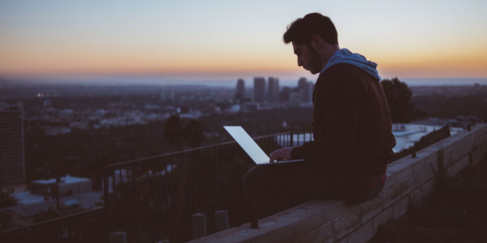 Remote Work Concept Image depicting a man working on a laptop sitting in isolation with a scenic background.