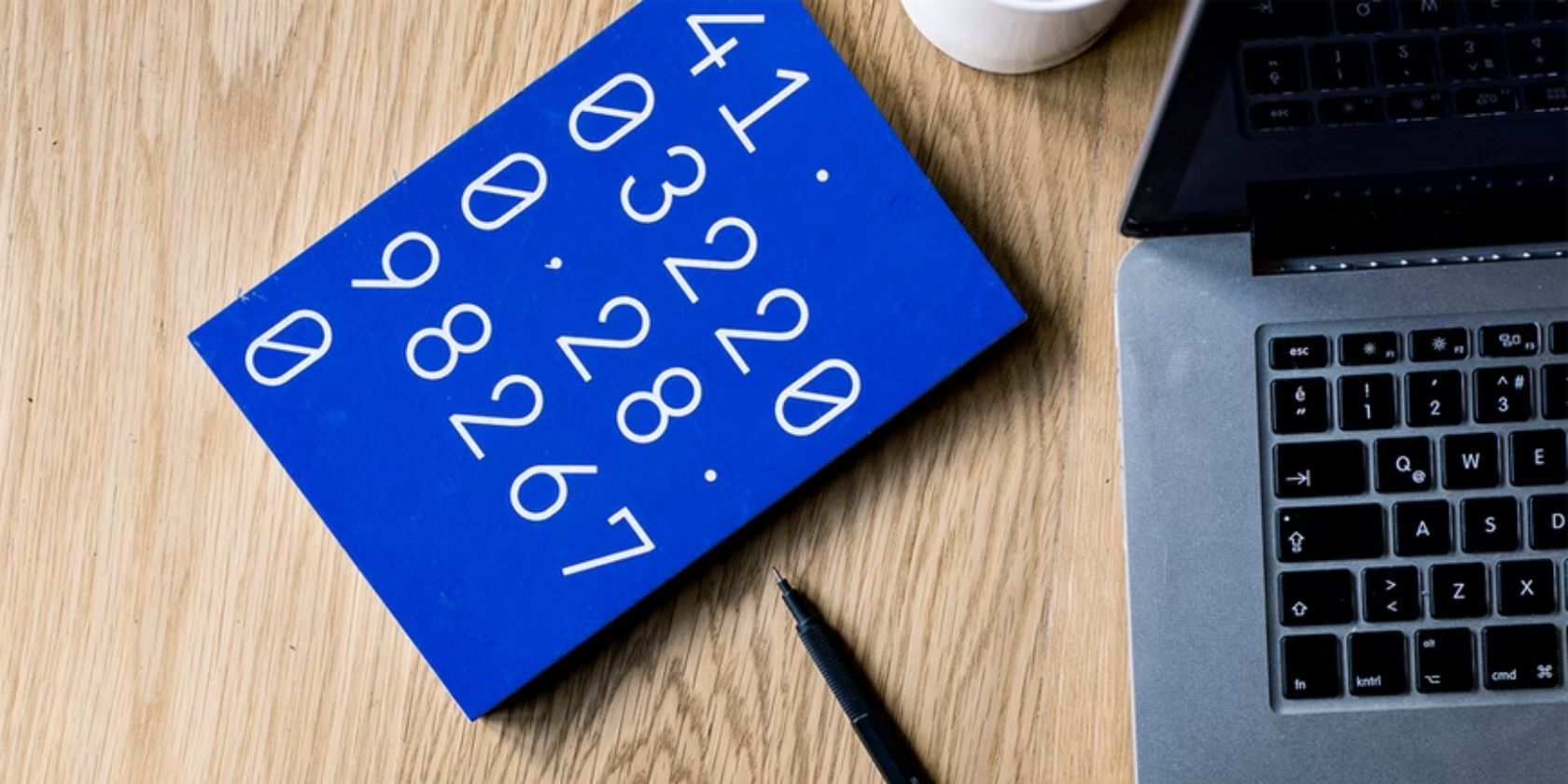 blue notebook with numbers on the cover placed next to laptop and pen on wooden surface