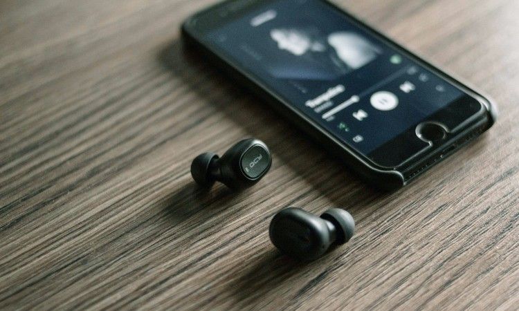 black-bluetooth-earbuds-sitting-next-to-black-phone-on-wooden-table