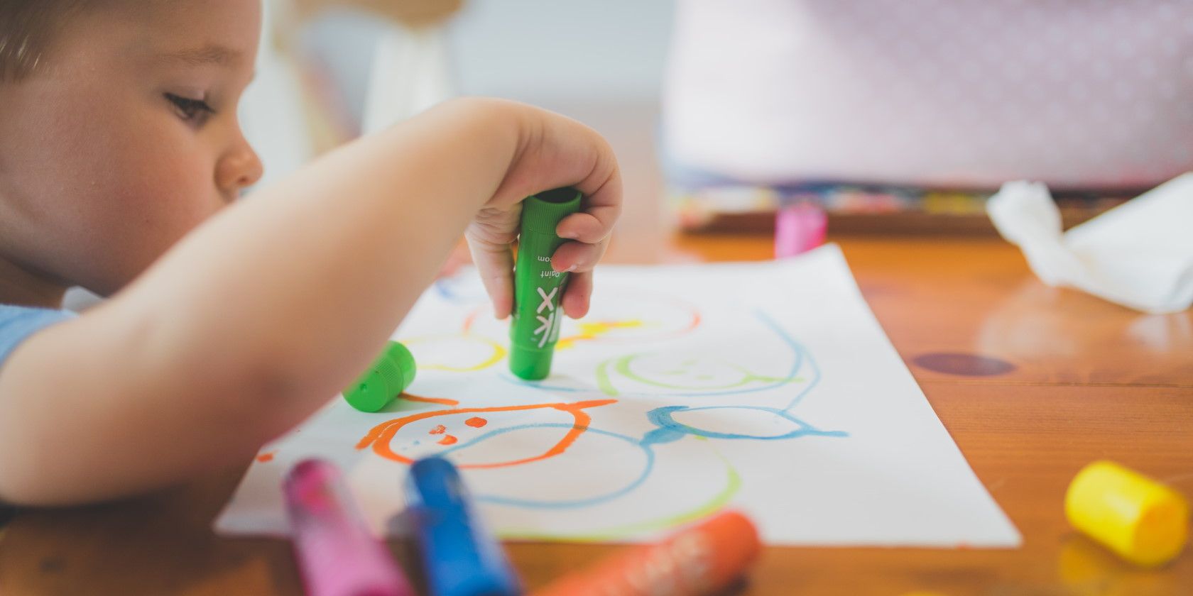 young child coloring on paper with green crayon