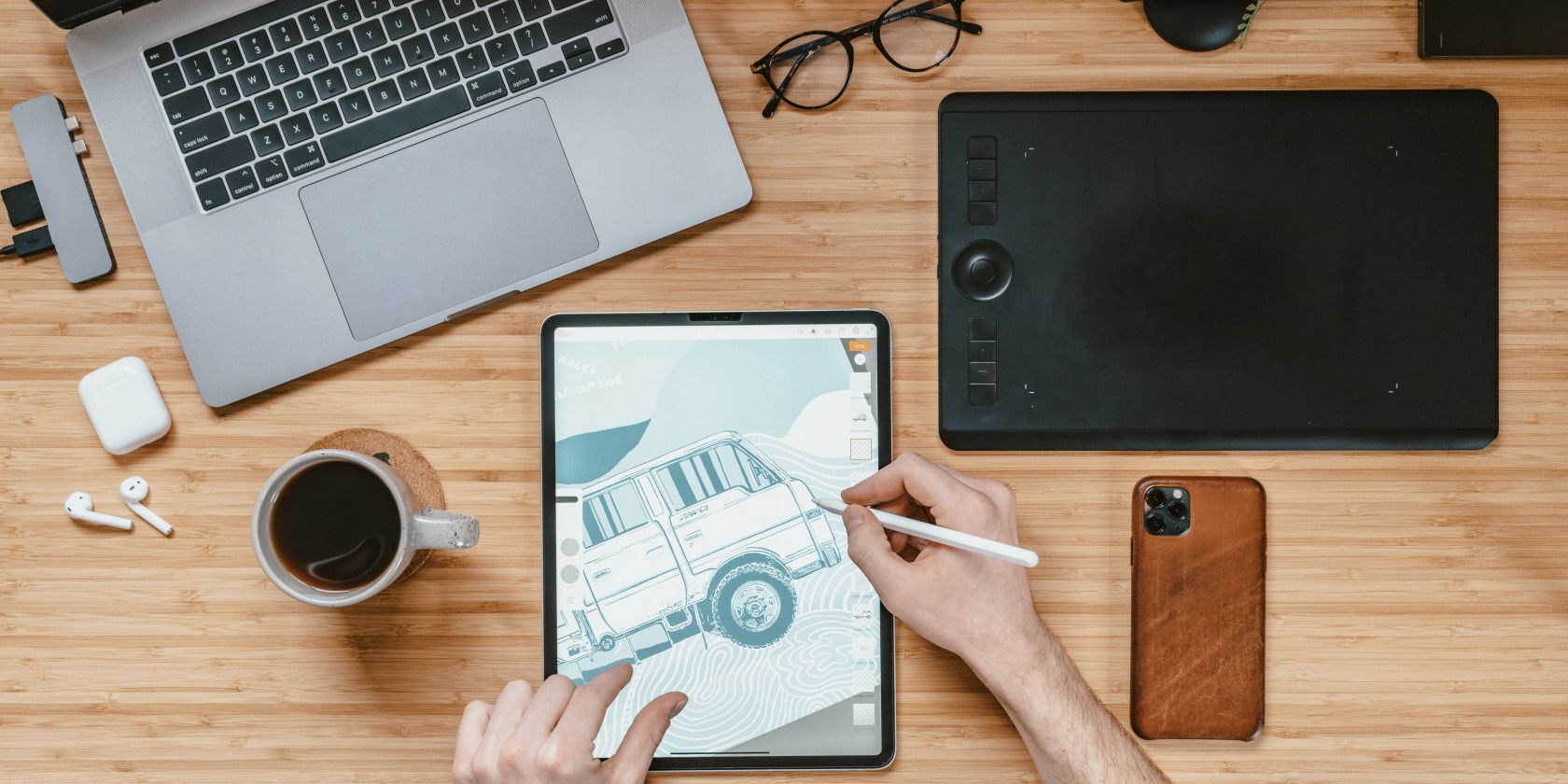 person sitting at desk next to laptop and smartphone drawing digital art