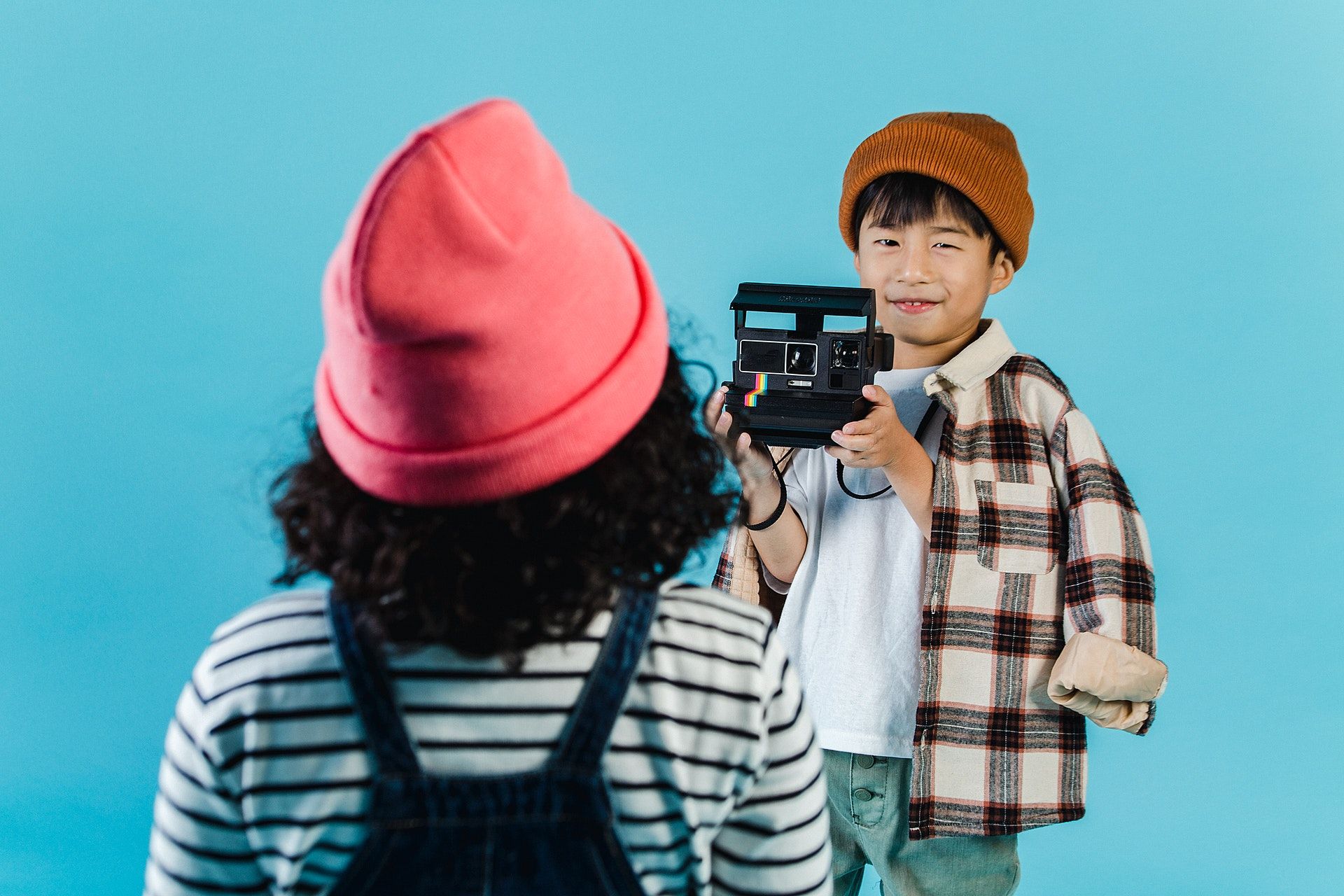 A child taking a picture of another child with a polaroid camera.