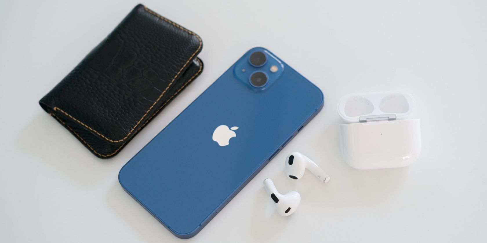 iPhone 13 next to a wallet and a pair of AirPods