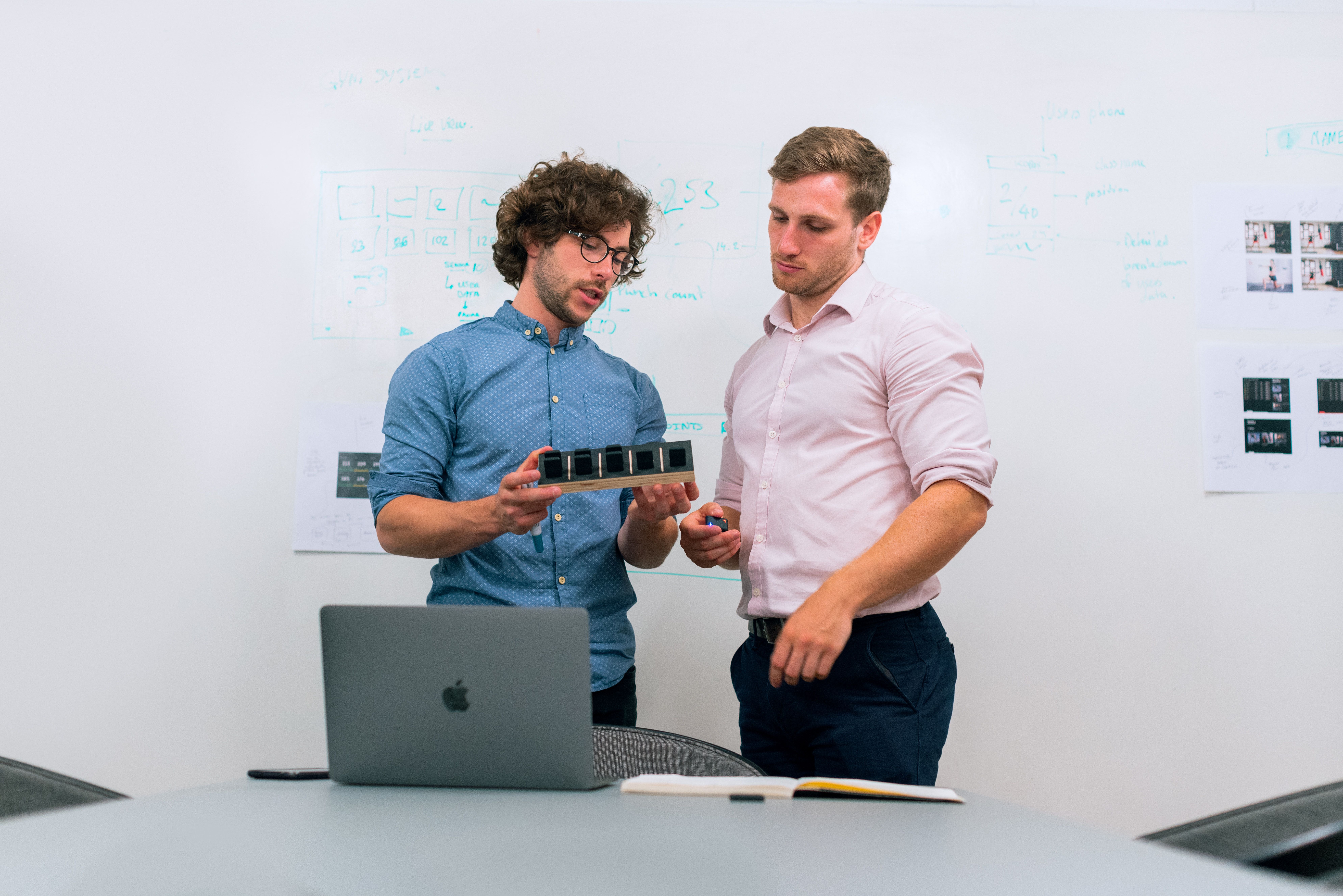 Two men standing near a laptop and they are looking at a prototype