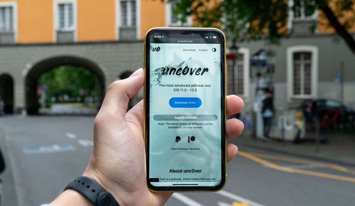 A hand holding an iPhone showing the Uncover jailbreak tool