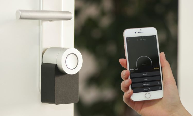 A person holding a white iPhone near a smart lock on a white door