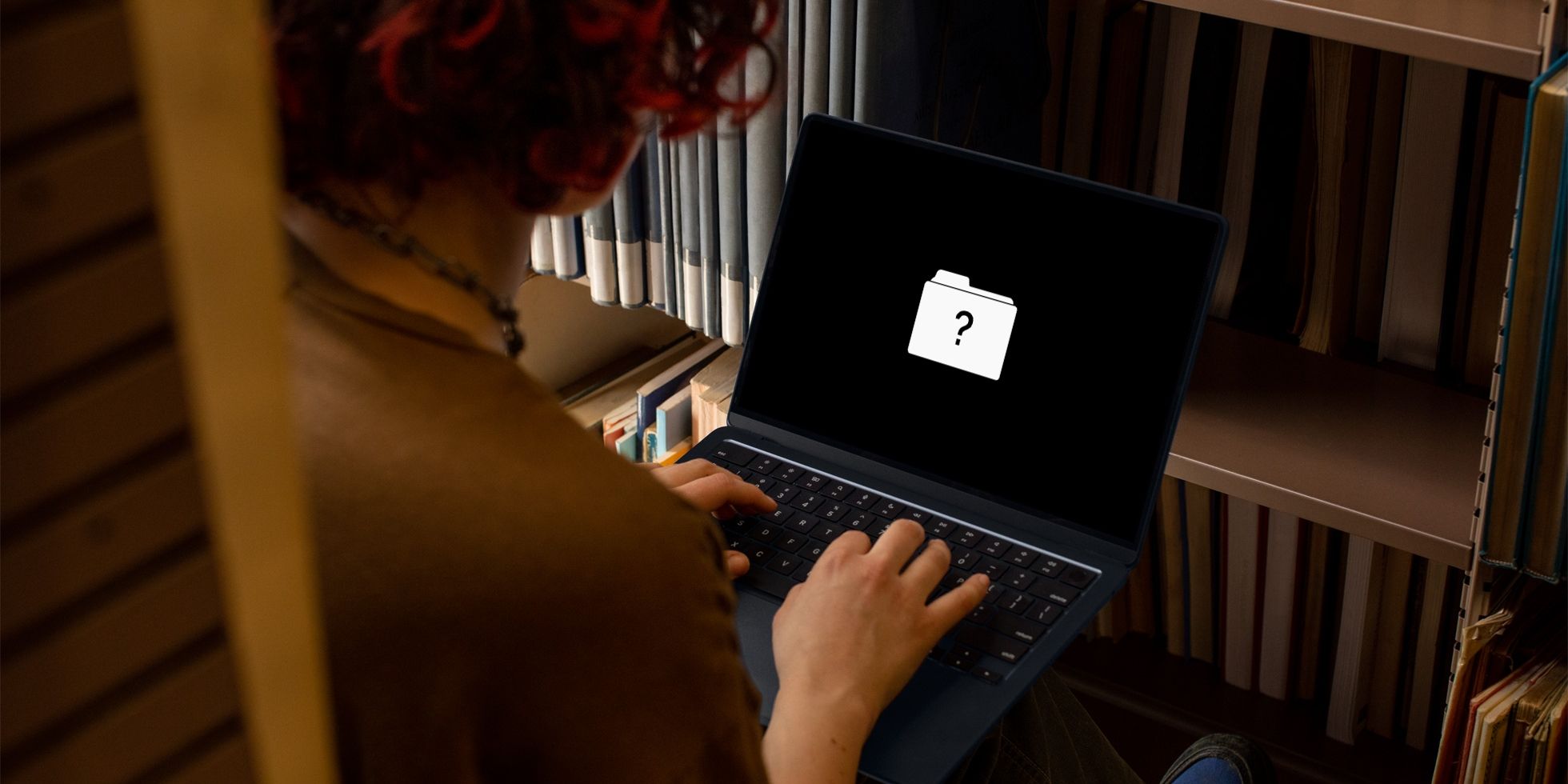 Una mujer sentada en su escritorio, solucionando problemas de una computadora portátil MacBook Air que muestra un signo de interrogación en la pantalla para advertir sobre un error en el disco de inicio