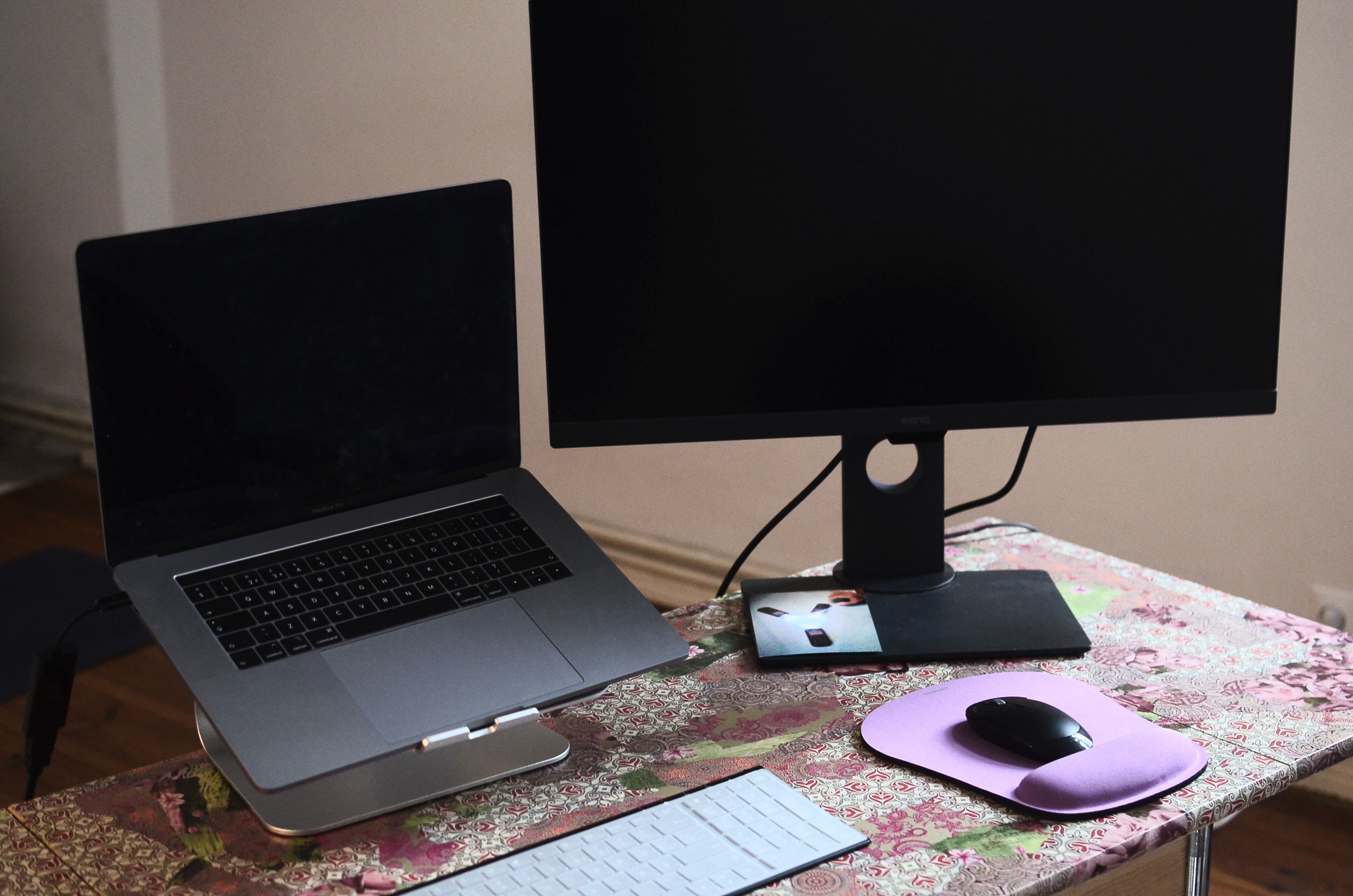 MacBook elevated on a metal stand on a desk with a keyboard and monitor