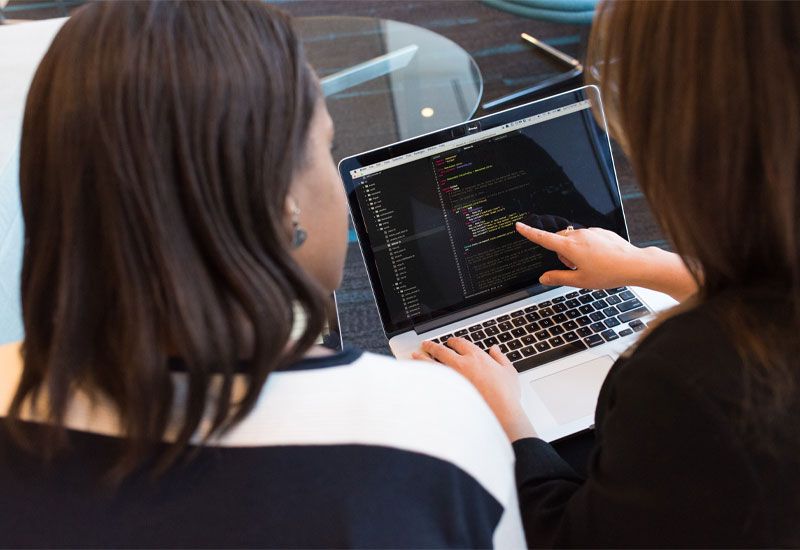 Two women looking at code on a laptop
