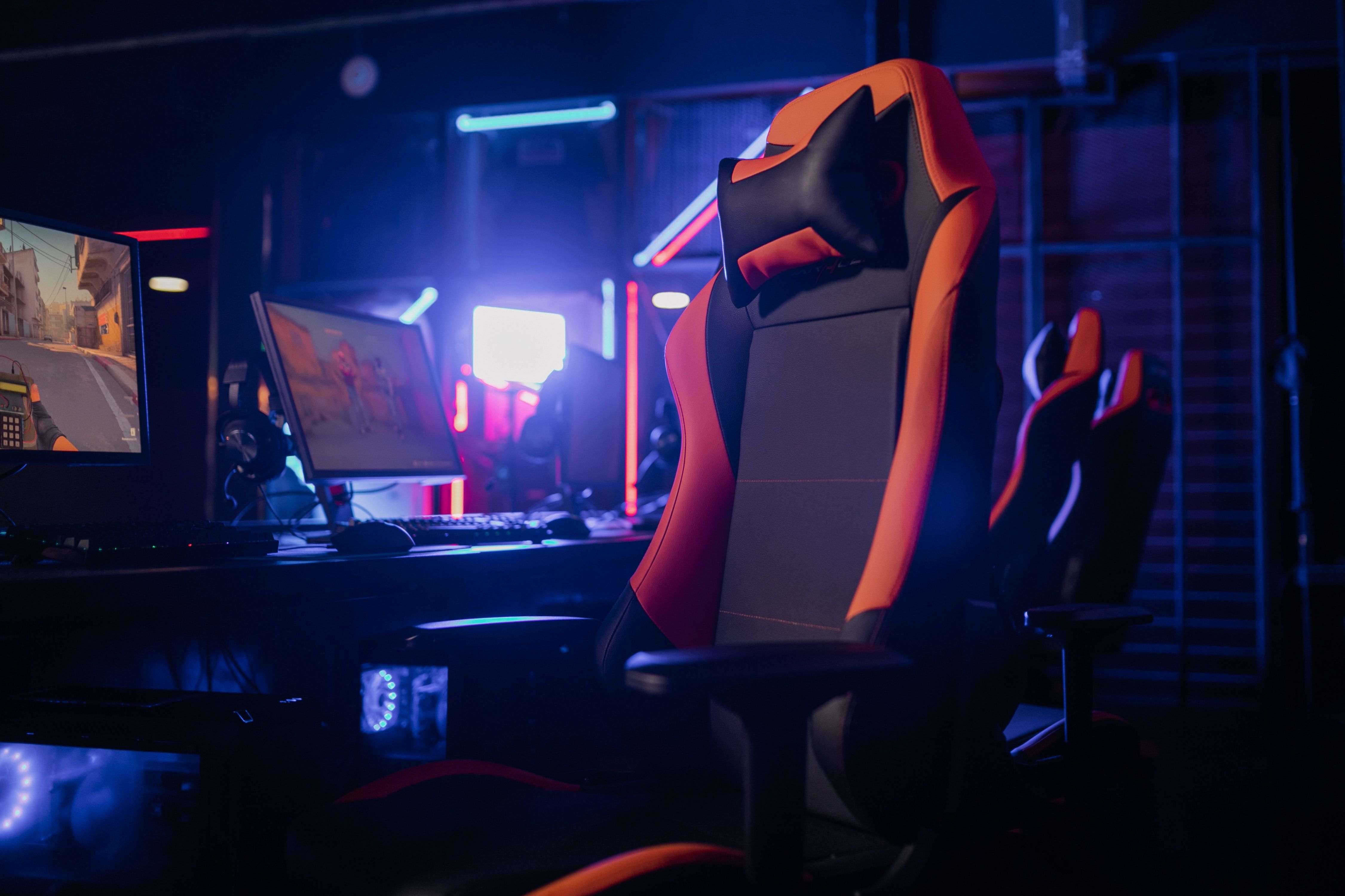 black and orange unbranded gaming chair in front of monitors and desktop pc