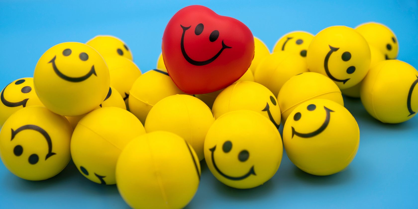 image of a range of smiley yellow emojis and a red heart emoji on a blue background
