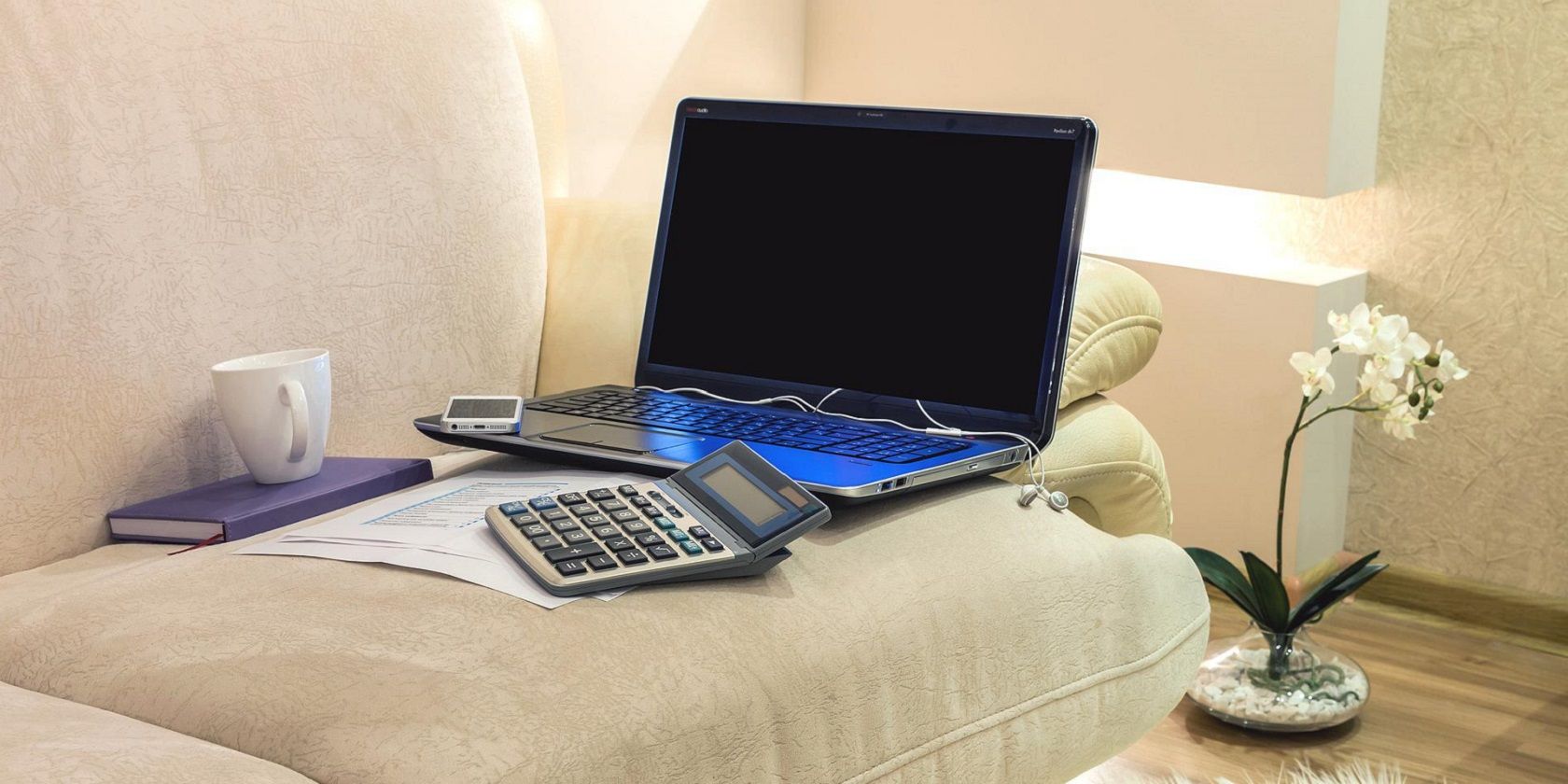 laptop on sofa with phone, calculator, notebook, and coffee mug
