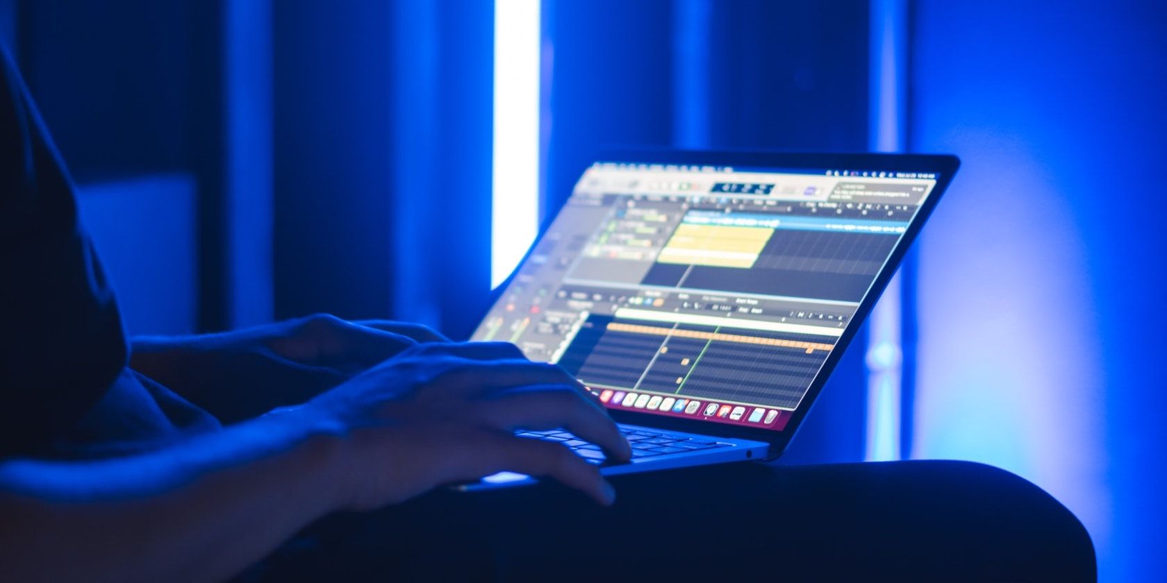 Человек, использующий GarageBand на ноутбуке под синим неоновым светом