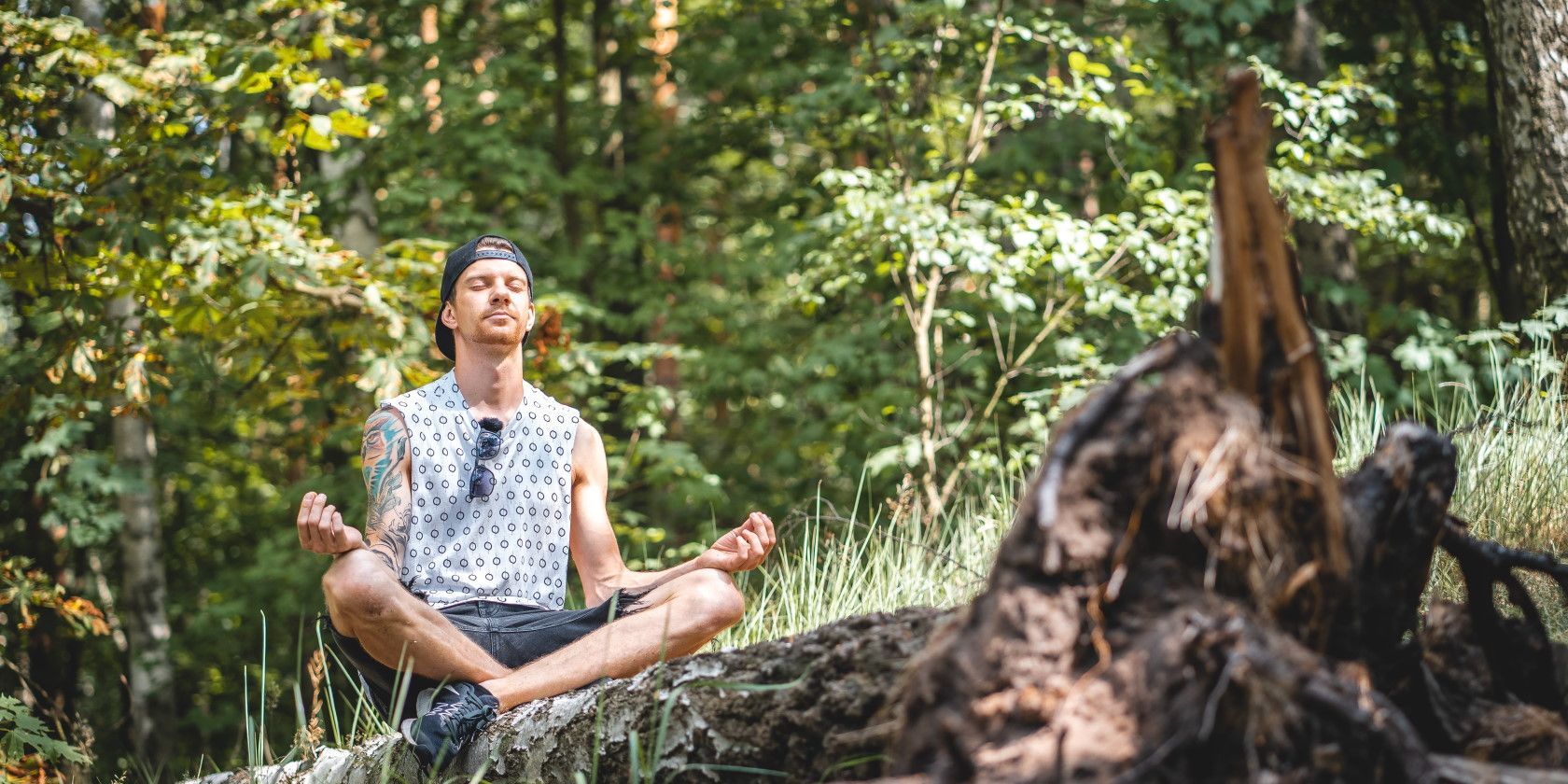 Man meditating in forest on a tree log