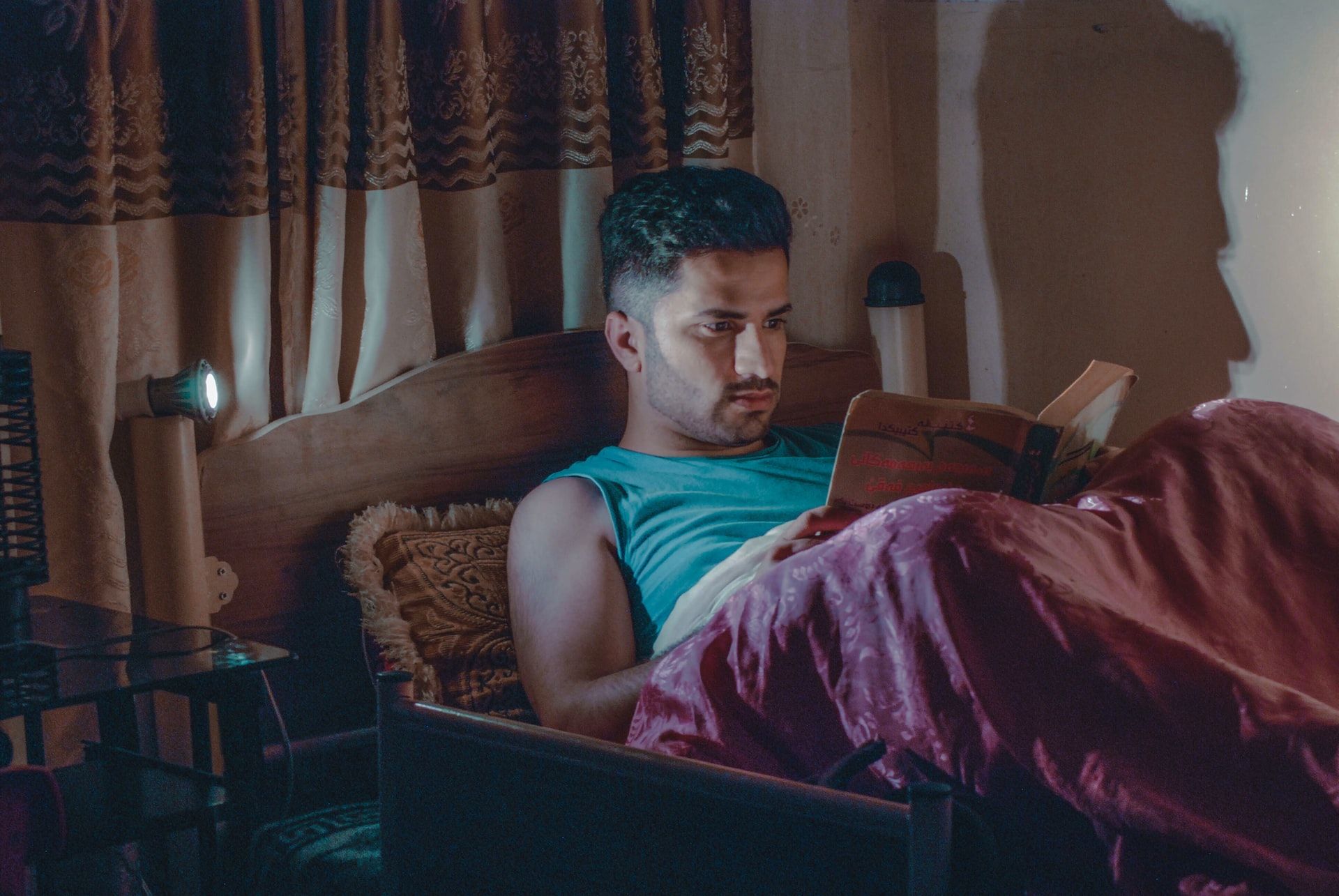man reading a book in bed with bedside lamp on