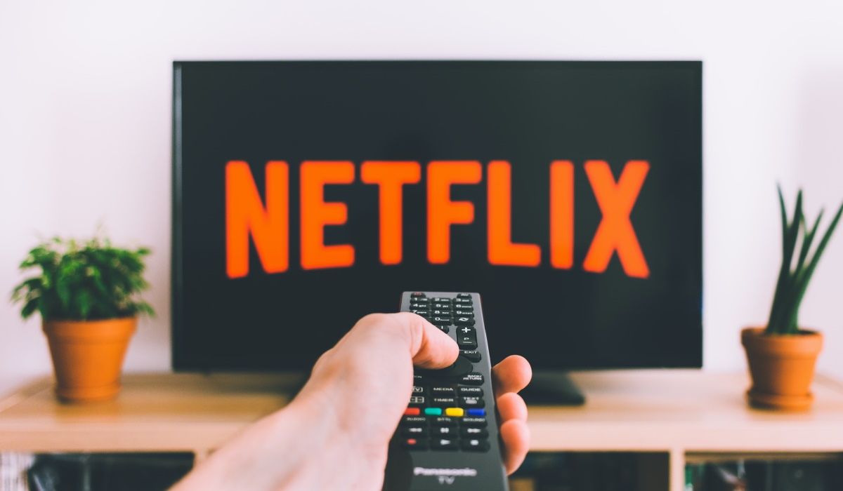 A hand holding a remote control and a TV showing the Netflix logo