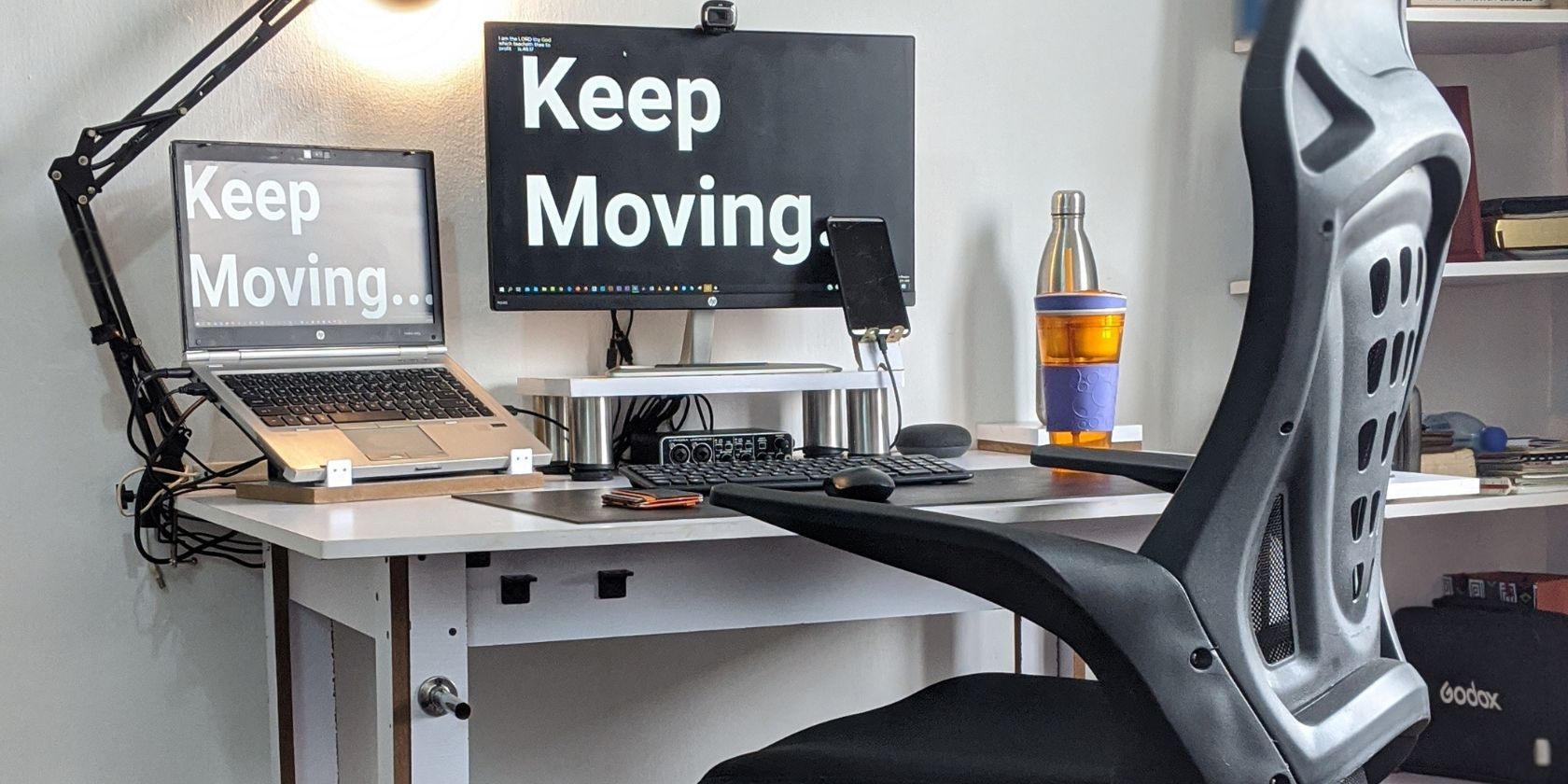 A chair in front of a desk with a monitor saying Keep Moving