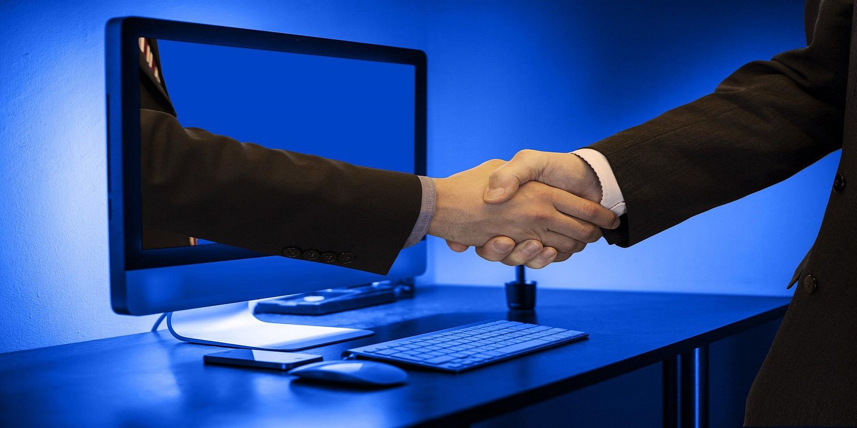 Hand reaching out of the computer to shake the hand of the person in front of it.