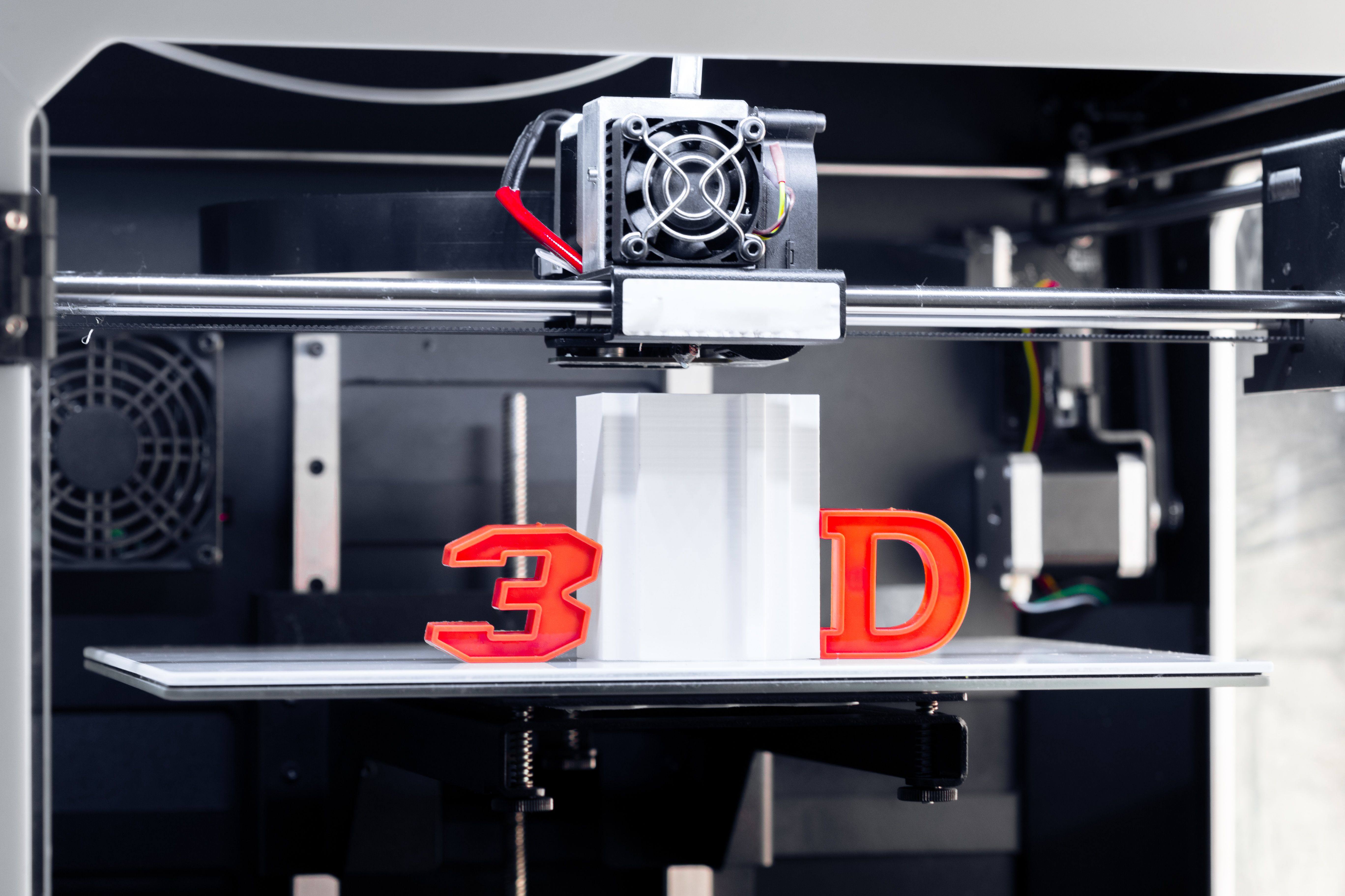 A 3D printer in action with letters 3D and D on both sides of a model being 3D printed in the build plate
