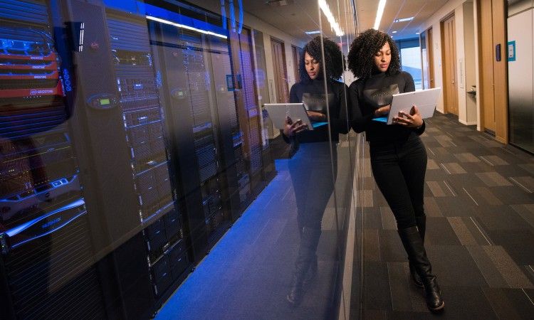 Woman holding laptop in hallway in front of servers