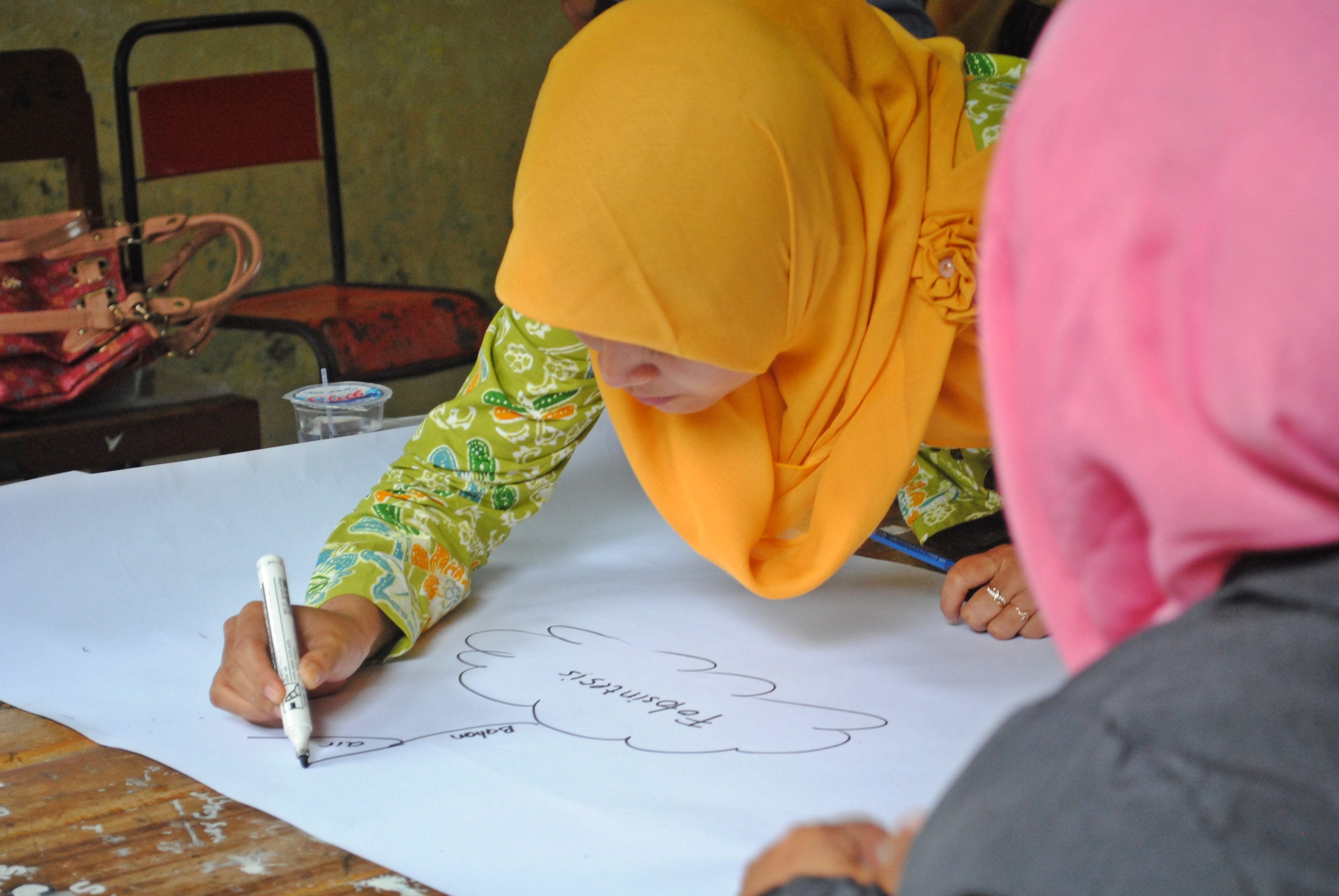 A hijabi person drawing a mind map on a broad sheet of paper