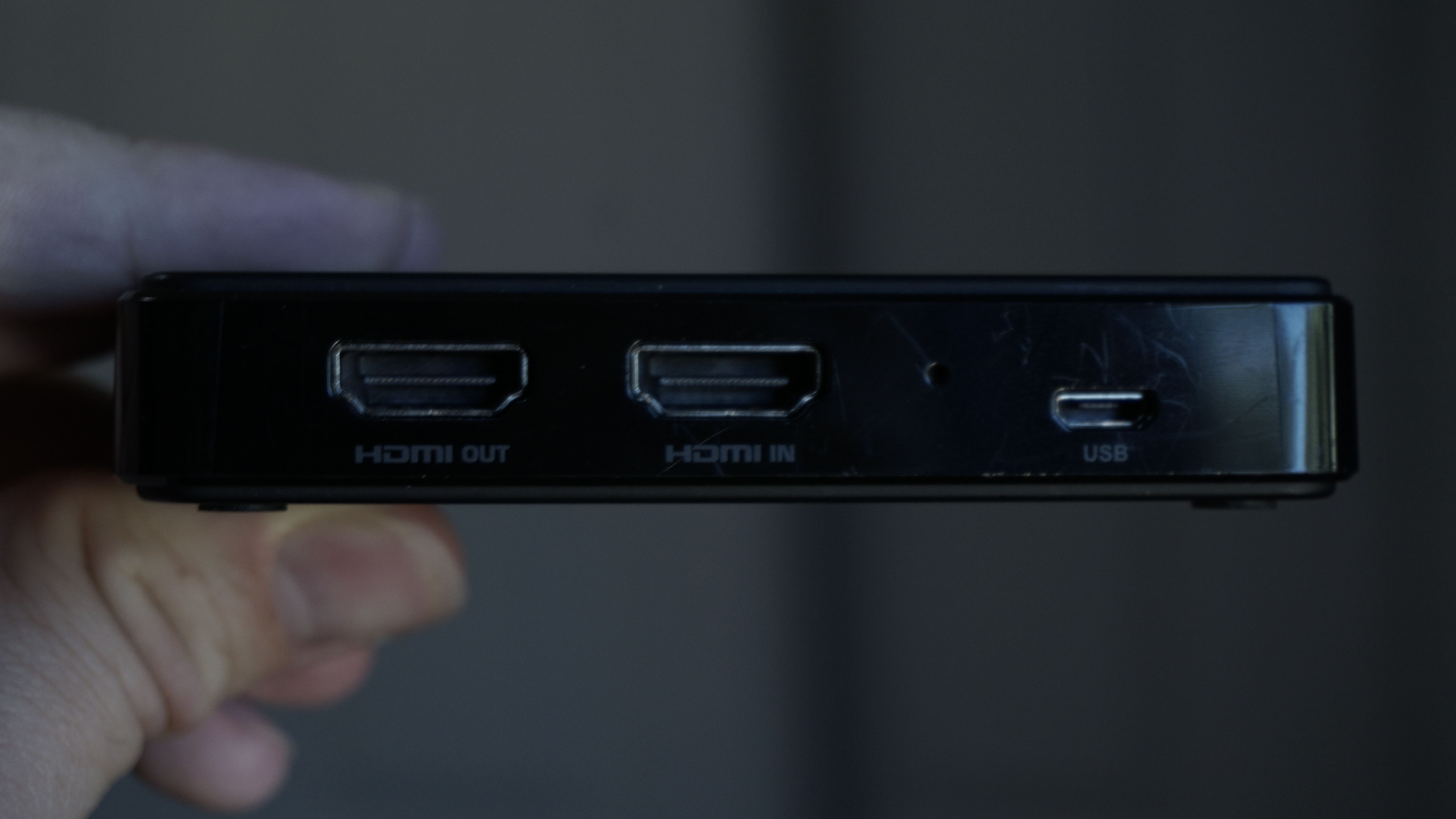 Holding a capture card and showing its HDMI in/out and USB ports