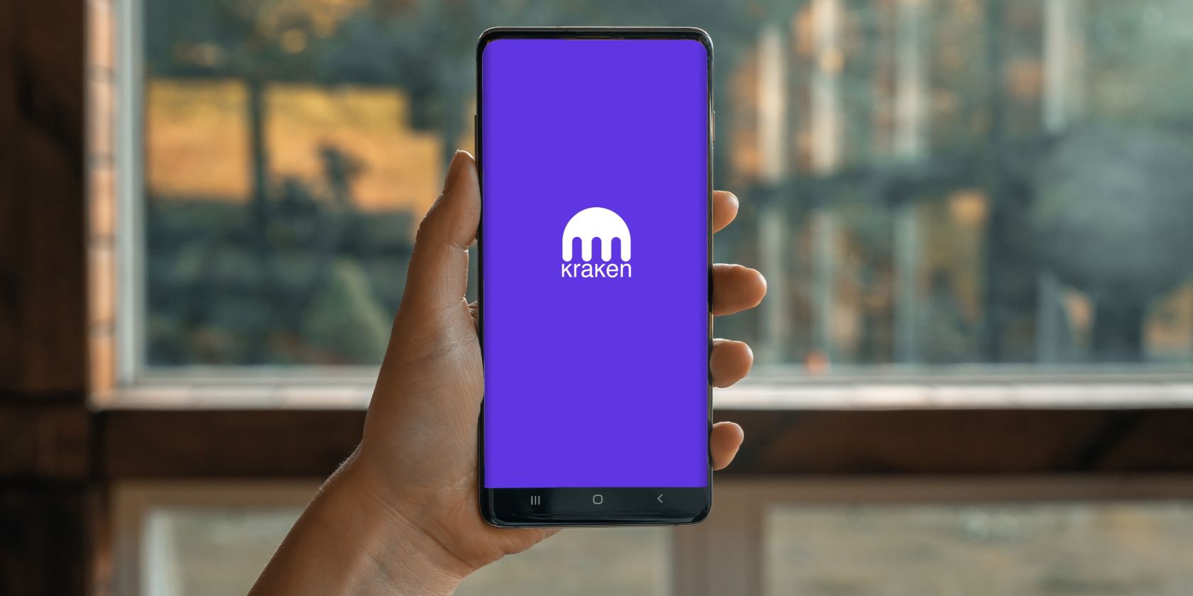 a hand holding a phone with kraken logo on the screen