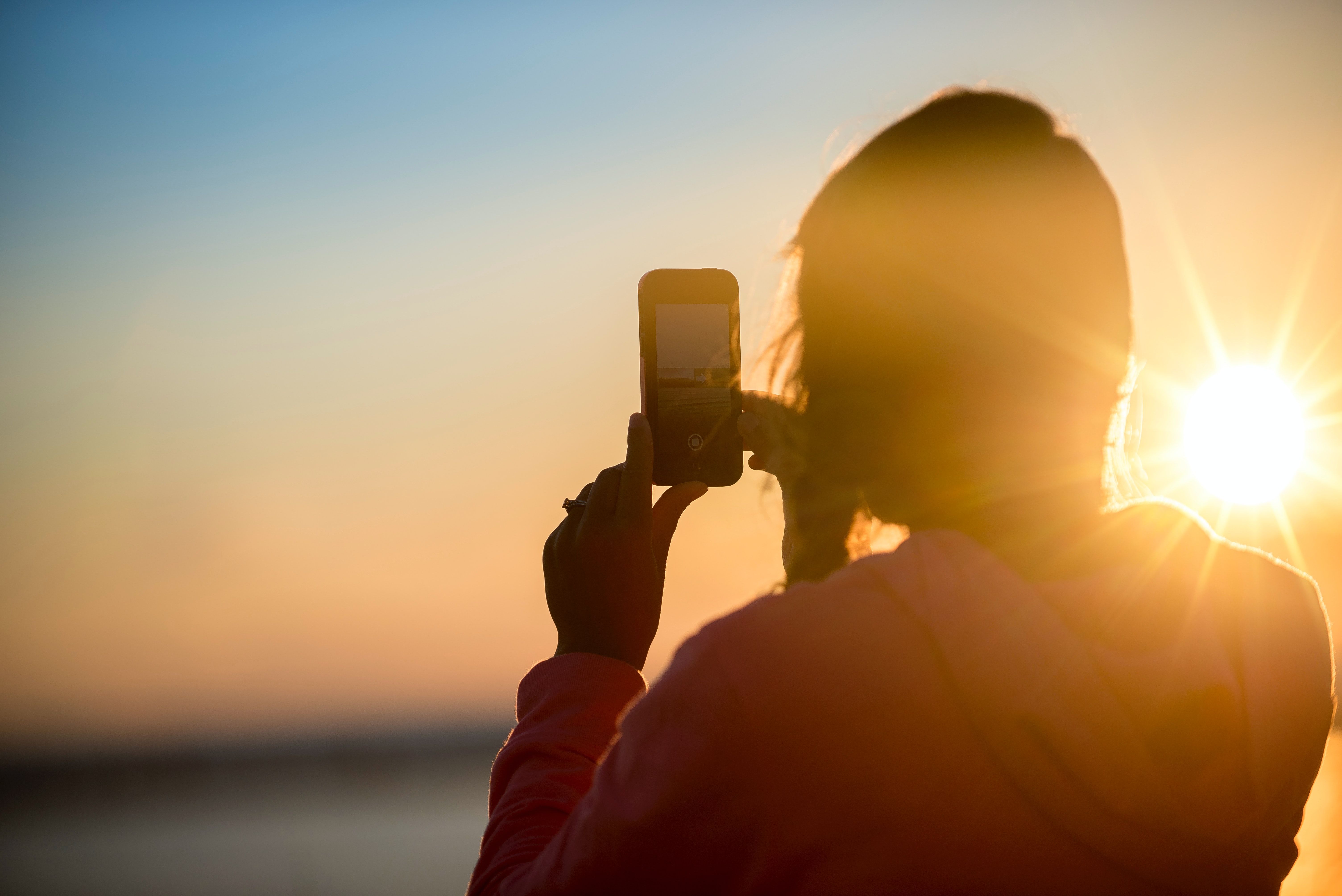 photo of someone taking pictures with smartphone at sunset