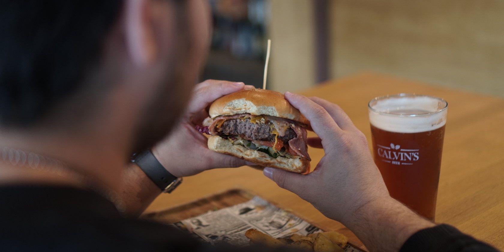 person eating beef bacon cheese burger with fries and beer