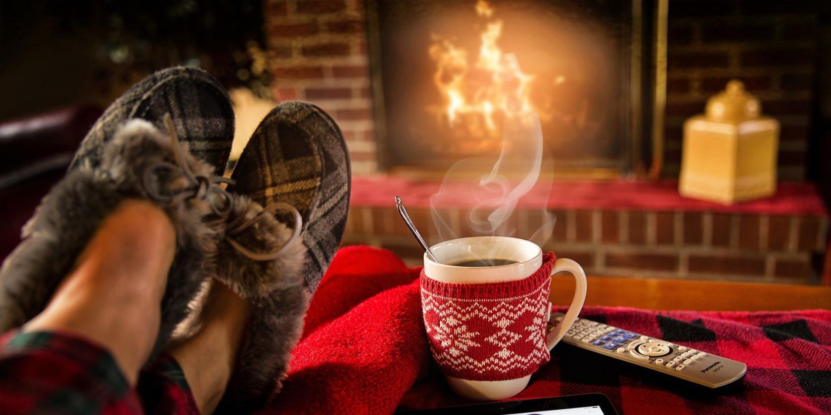 A person lounging in front of a fireplace with their feet up and a hot drink next to them