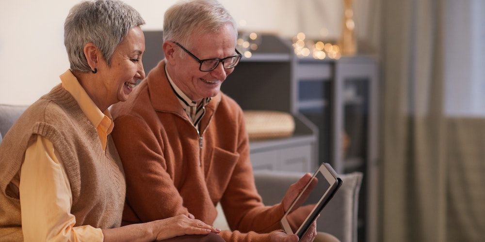 old couple smiling while watching something on a tablet