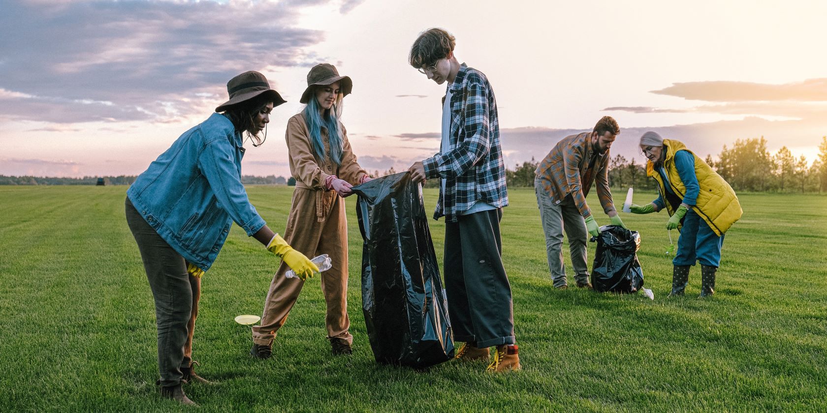 Five people in a grassy field collecting garbage in bin bags