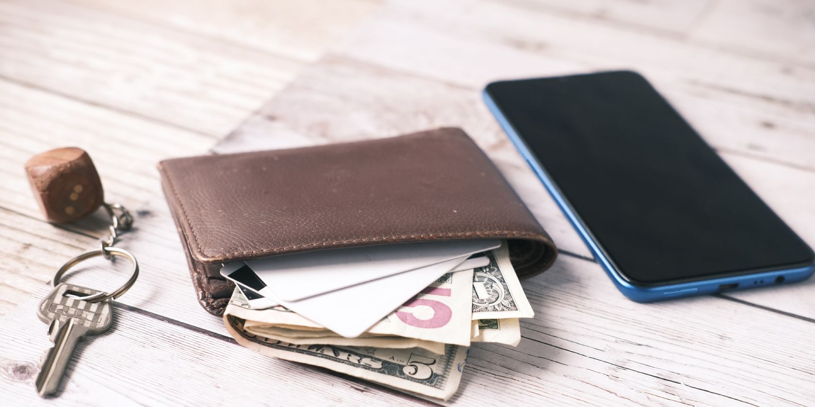 picture of a leather wallet with currency bills on it, on a table with a key and smart phone