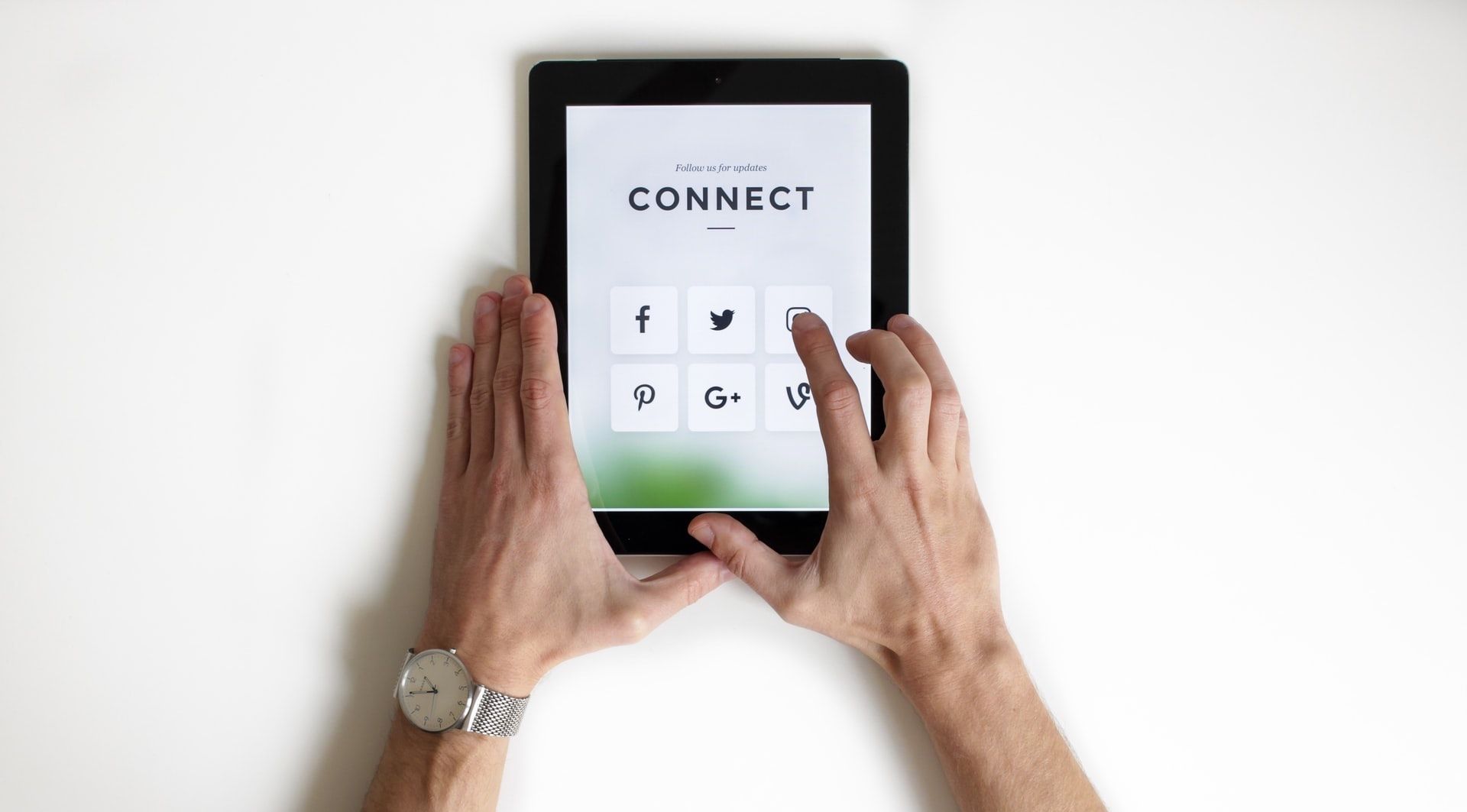 Two hands using an ipad displaying different types of social media icons.