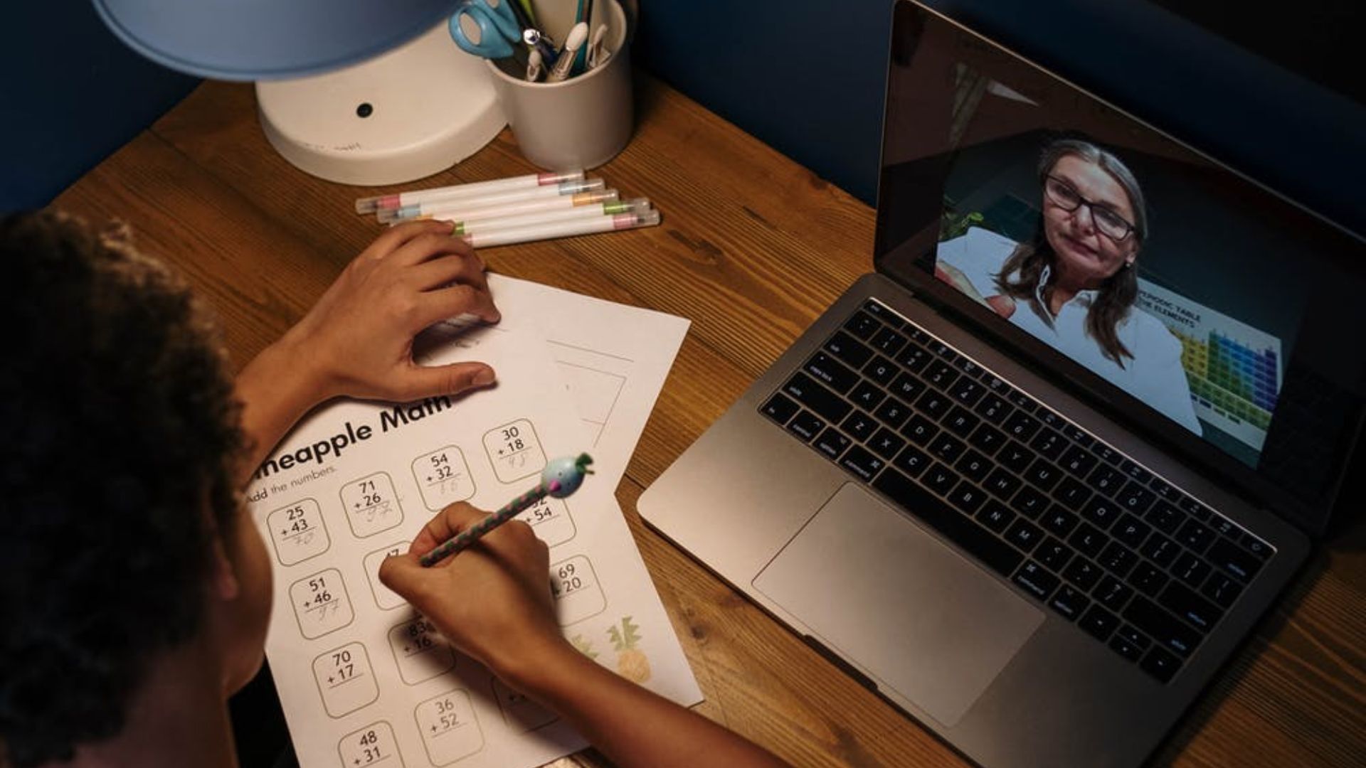 student working on a math worksheet with his teacher on a video call