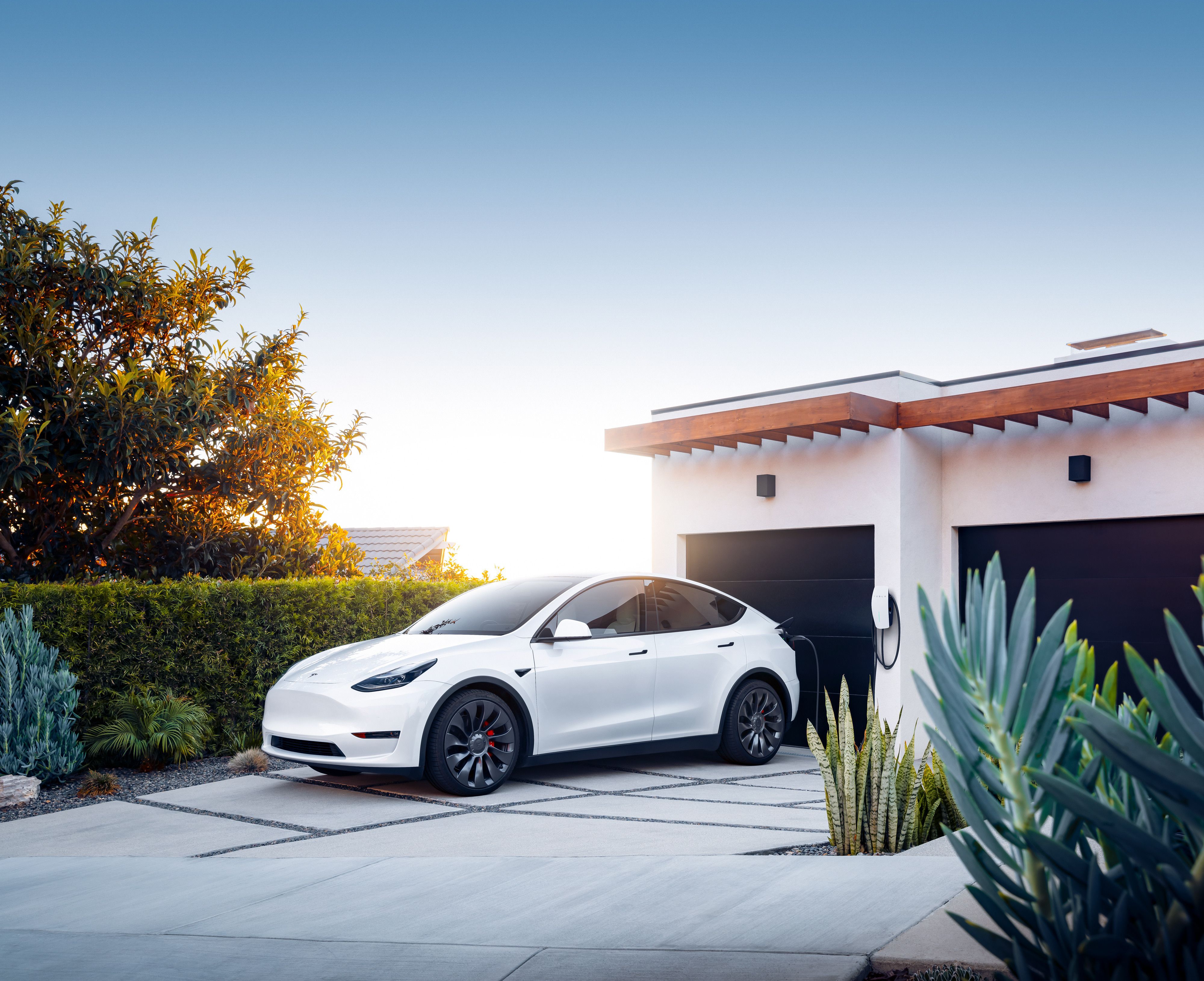 A white Tesla plugged into a home charging station