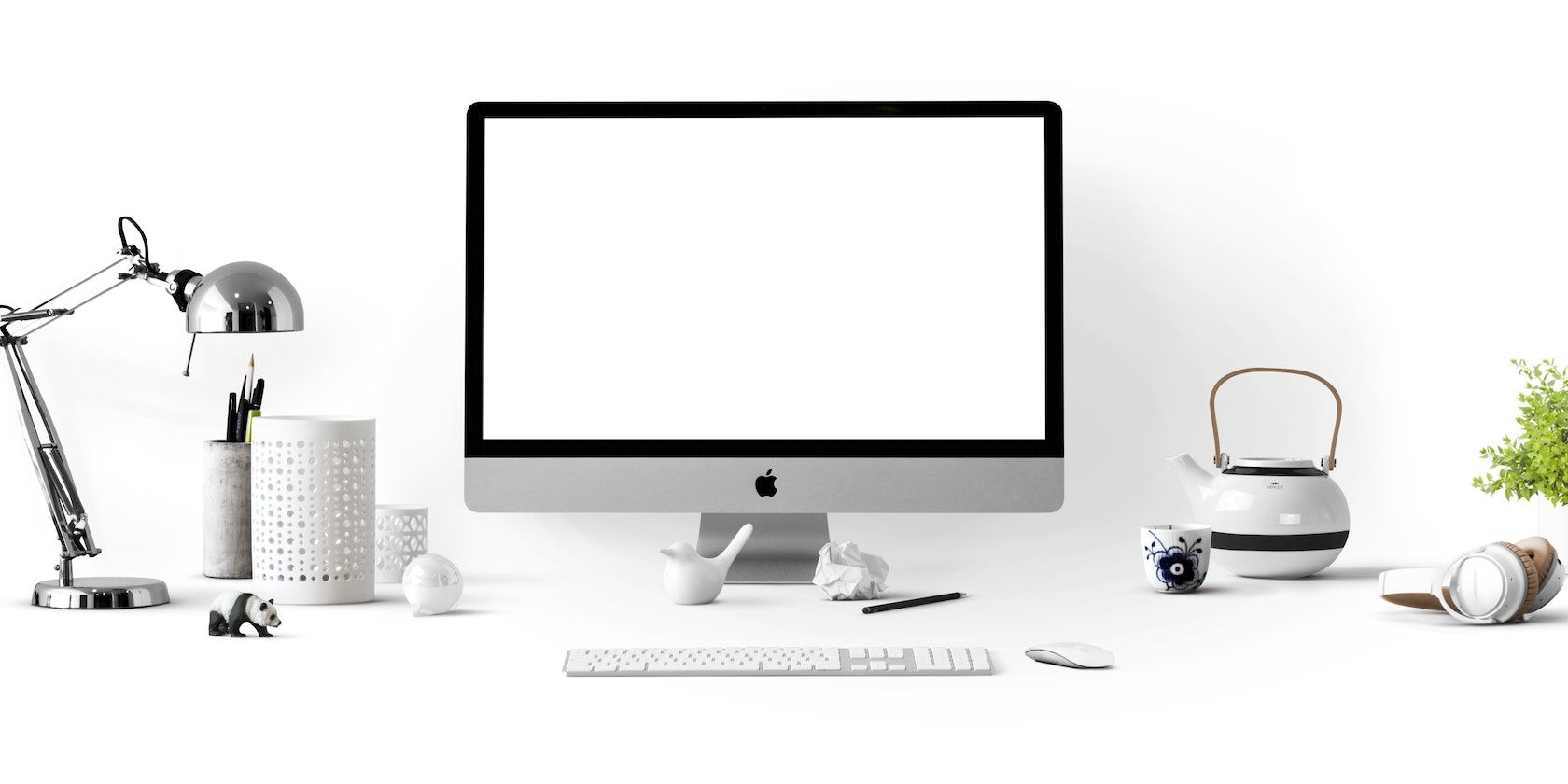 A silver iMac surrounded by a ceramic kettle and a collection of work gadgets