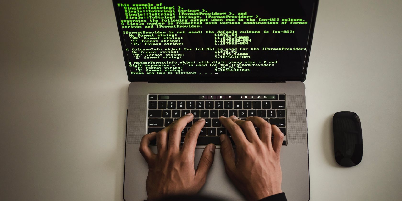 Pemandangan dari atas tangan mengetik di laptop dengan kode pemrograman berwarna hijau ditampilkan di layar