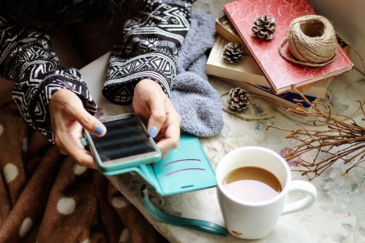 Woman&rsquo;s hand handling a phone with a cup of coffee