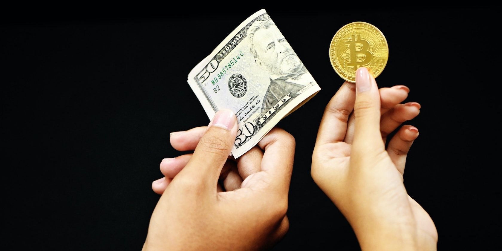 Hand holding $50 bill, with another hand holding a Bitcoin