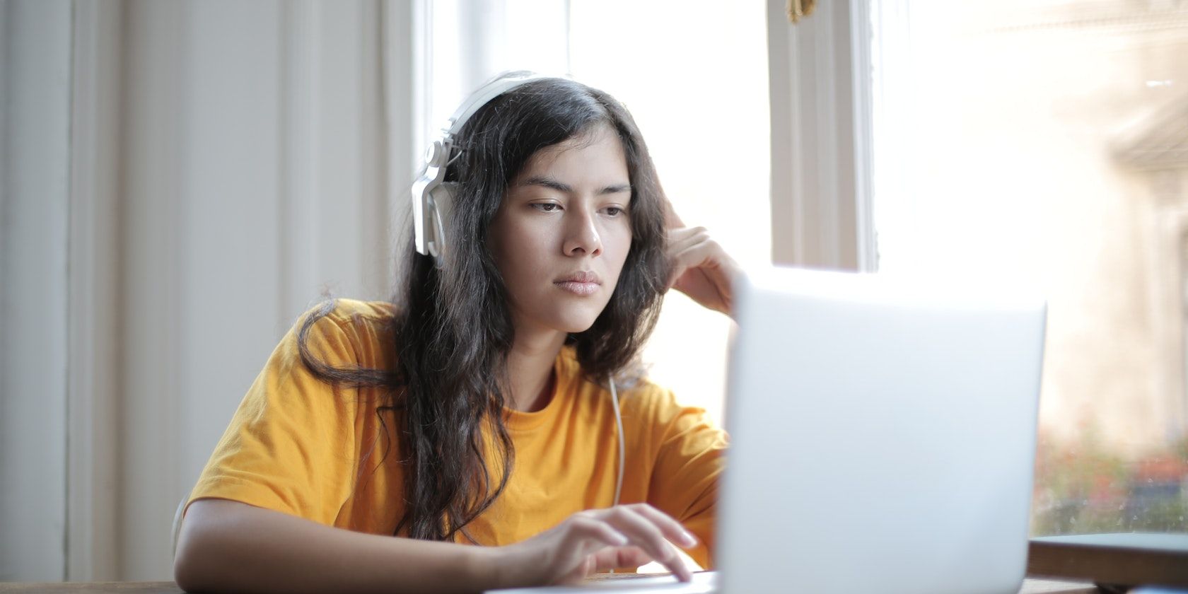 Woman in yellow shirt wearing headphones and using MacBook