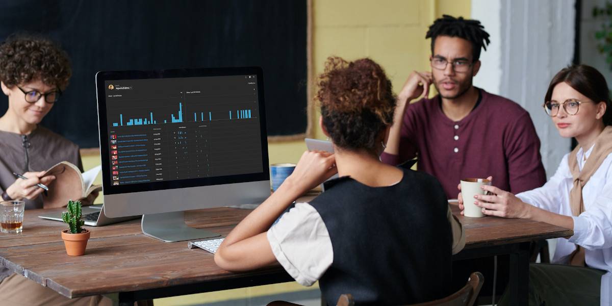 Woman looking at Live YouTube Analytics on a monitor and discussing with others
